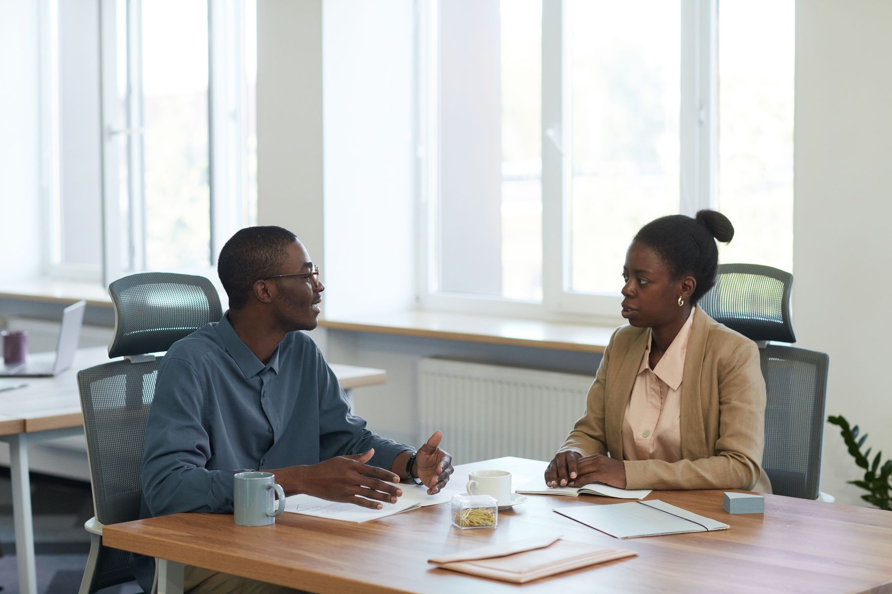 Two people in conversation across a wooden table with notebooks.